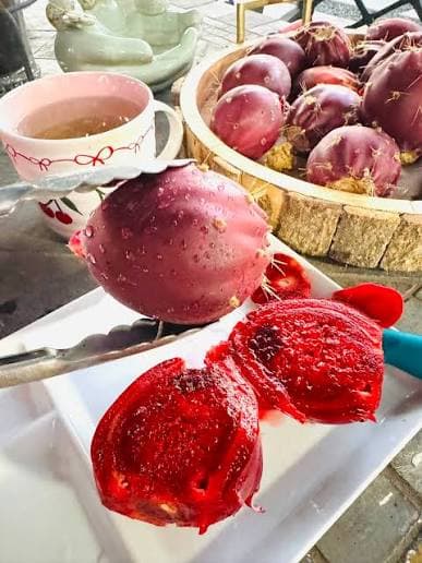 Freshly sliced prickly pear fruit on a white plate with a wooden bowl of whole cactus pears in the background